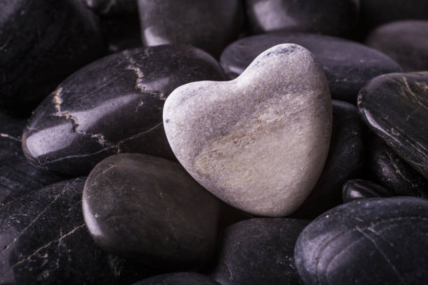 Color photo of a heart-shaped stone sitting amongst other rocks on the beach.