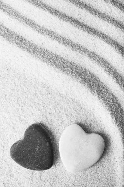 two stone-shaped hearts one white and the other black on pink sand