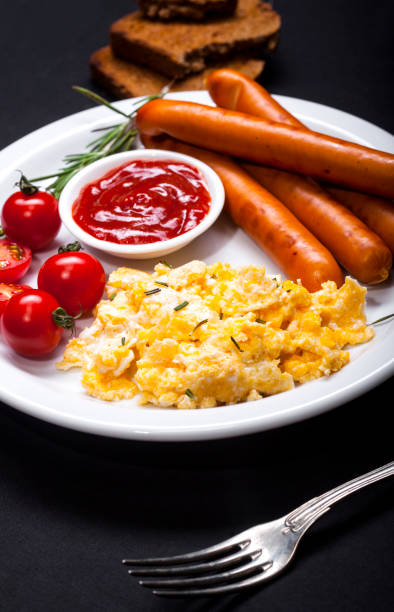 istock Wiener Sausages and scrambled eggs in a dish on black background. 972102036