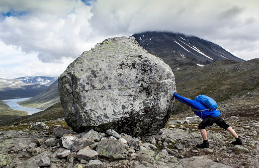 The guy is pushing a big rock in the mountains. Traveling in Norway.