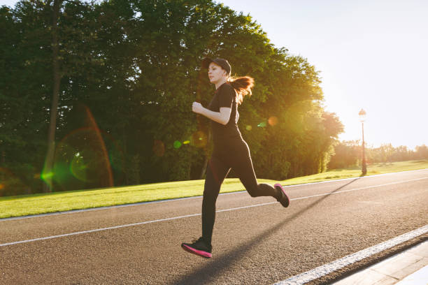istock Young athletic girl in black uniform and cap training, doing sport exercises, running, looking straight on path in city park outdoors on spring or summer sunny day. Fitness, healthy lifestyle concept. 972154898