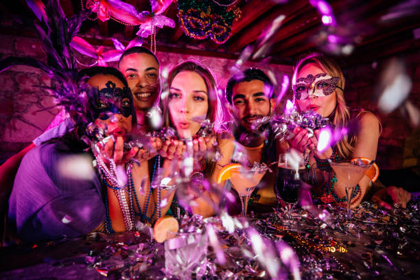 Happy friends celebrating Mardi Gras and blowing confetti at party Young multi-ethnic friends having fun with drinks and blowing confetti at Mardi Gras bar party mardi gras confetti stock pictures, royalty-free photos & images