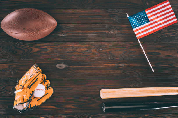 вид сверху на нас флаг, регби мяч, бейсбольные биты и перчатки с мячом на деревянном столе - baseball baseball bat baseballs patriotism стоковые фото и изображения