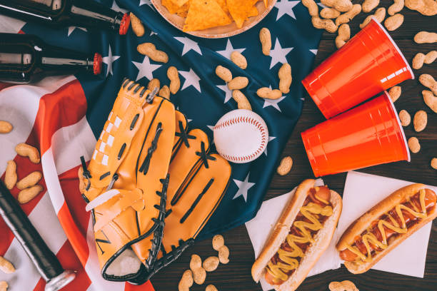 widok na hot dogi, plastikowe kubki, orzeszki ziemne, butelki po piwie, piłkę baseballową i rękawiczki z kijem na amerykańskiej fladze - baseball baseballs peanut american culture zdjęcia i obrazy z banku zdjęć