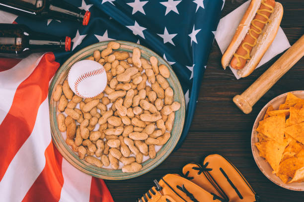 vue de dessus de la balle de baseball sur plaque avec arachides, batte de baseball, gant, hot dogs et des bouteilles de bière sur le drapeau américain - baseball baseballs peanut american culture photos et images de collection