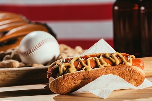 close-up view of hot dog, baseball bat and sport equipment on wooden table
