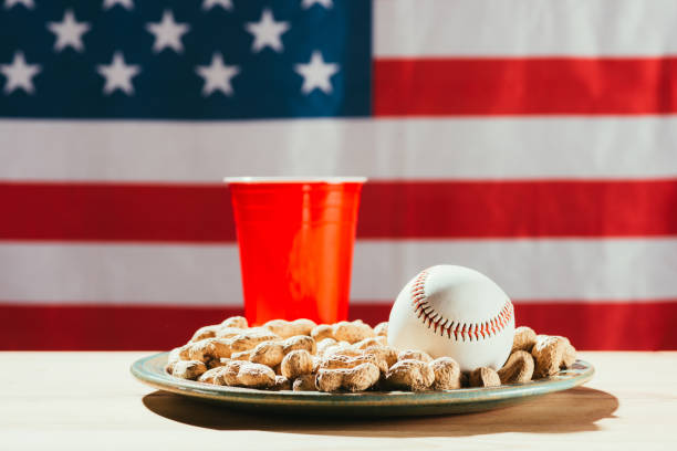 zbliżenie piłki baseballowej na talerzu z orzeszkami ziemnymi, czerwoną plastikową butelką i amerykańską flagą za - baseball baseballs peanut american culture zdjęcia i obrazy z banku zdjęć