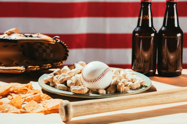 zbliżenie piłki baseballowej na talerzu z orzeszkami ziemnymi, butelkami z kijem i piwem, skórzaną rękawicą i amerykańską flagą - baseball baseballs peanut american culture zdjęcia i obrazy z banku zdjęć