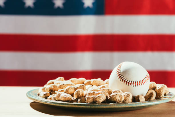 vue rapprochée de la balle de baseball sur la plaque avec les arachides et le drapeau américain derrière - baseball baseballs peanut american culture photos et images de collection