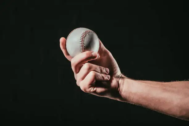 Photo of close-up partial view of male hand holding baseball ball isolated on black