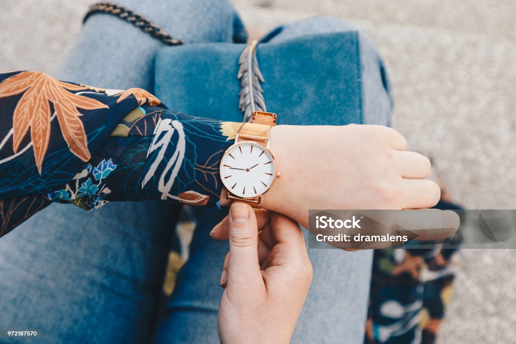 close up, young fashion blogger wearing a floral jacker, and a white and golden analog wrist watch. checking the time, holding a beautiful suede leather purse. street style fashion details Watch - Timepiece Stock Photo