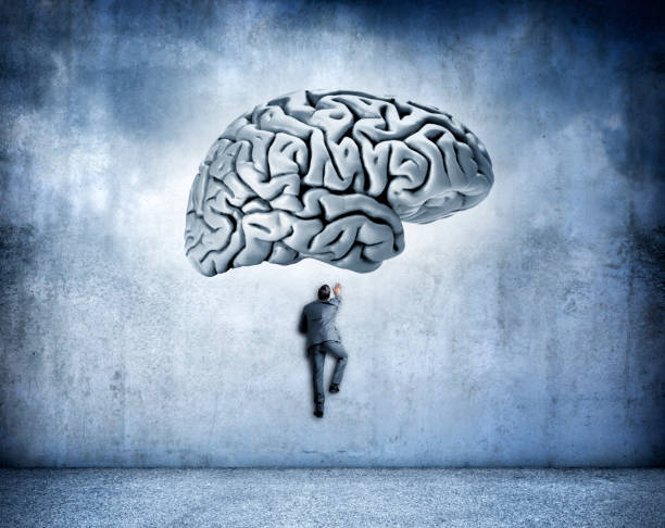 istock Man Climbing Wall Toward Large Human Brain Above Him 972253096