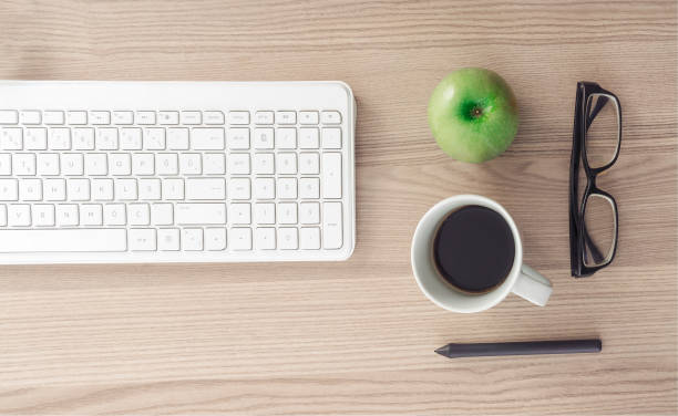 istock Office Desk with computer keyboard, coffee, pen, apple and eyeglasses 972291516