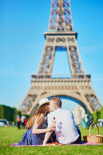 Romantic couple having picnic on grass with wine and fruits near the Eiffel tower in Paris