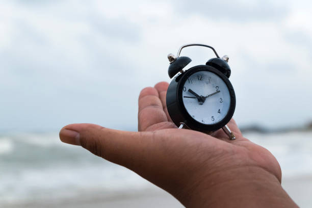 istock hand holding vintage alarm clock over sandy beach background 972318408