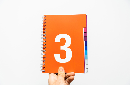 Male hand holding notebook with big number 3 printed on orange color ready for presentation or business quote, etc