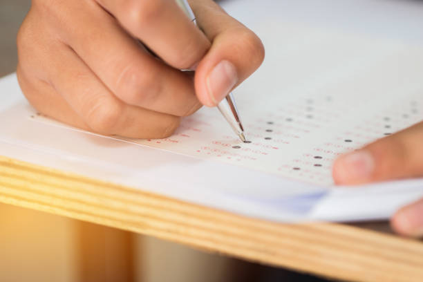 istock Education test concept : Hands student holding pen for testing exams writing answer sheet or exercise for taking fill in exam carbon paper computer on wood table at classroom in high school 972364302
