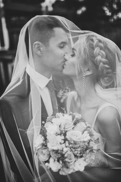 Romantic wedding moment, couple of newlyweds kissing under the veil in nature in the park. Black and white photo. Romantic wedding moment, couple of newlyweds kissing under the veil in nature in the park. Black and white photo. veil photos stock pictures, royalty-free photos & images