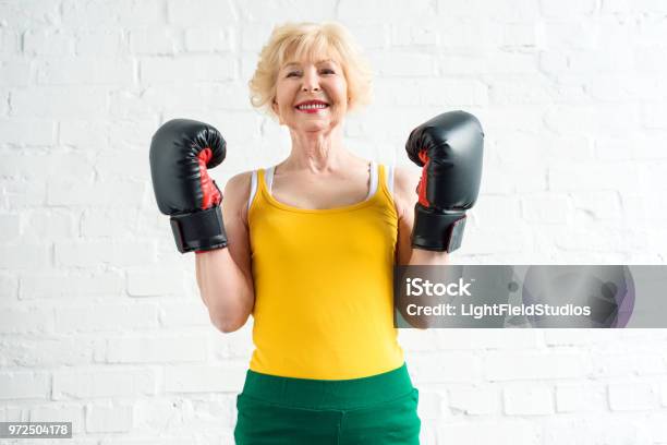 Feliz Mujer Senior Deportiva En Guantes De Boxeo Sonriendo A Cámara Foto de stock y más banco de imágenes de Boxeo - Deporte