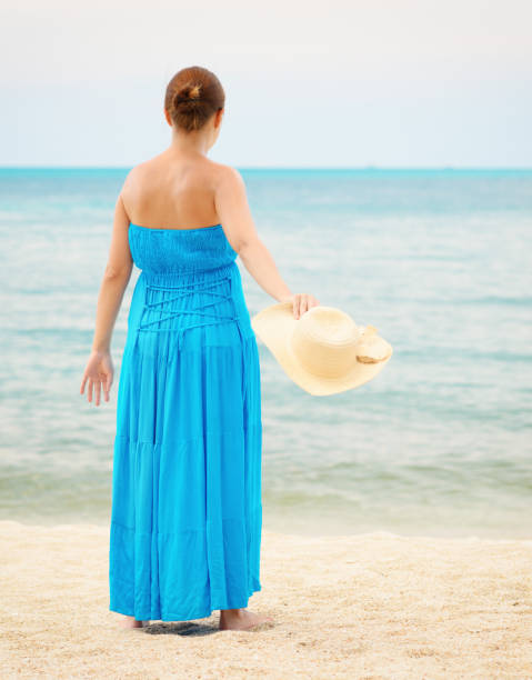 istock Woman in blue dress throws hat on the beach 972520630