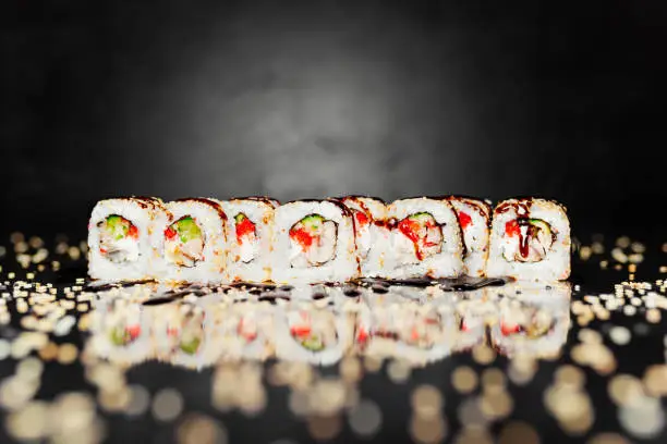 Sushi roll Philadelphia unagi on black background made of Seaweed, marinated rice, sesame seeds, cheese Philadelphia, cucumber, roasted eel, masago caviar, unagi sause. Pickled ginger, wasabi, soy sause. Sushi menu. Japanese food. Free-space. Close-up.