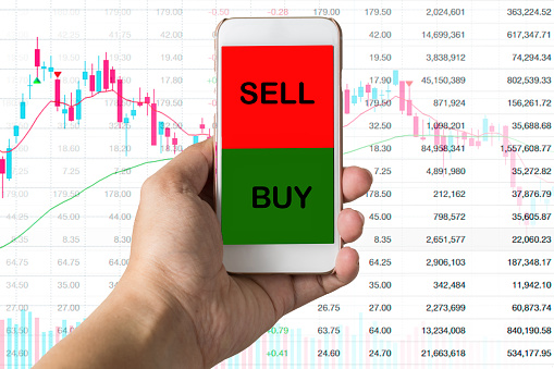 hand holding mobile trading stock by using smartphone with background blending by stock graph and city light.