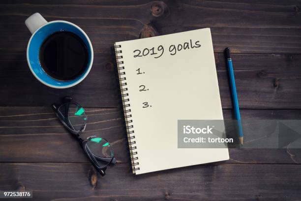 Notebook With 2019 Goals Massage Pencil Glasses And Cup Of Coffee On Wood Background Stock Photo - Download Image Now