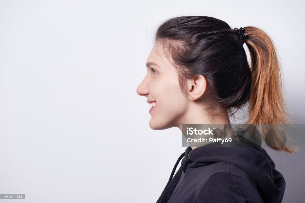 Side view of smiling woman looking forward Side view closeup of smiling woman standing by white wall looking forward Profile View Stock Photo