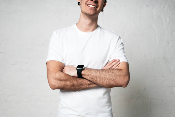 istock Smiling young man wearing blank white t-shirt and smartwatch, empty wall, horizontal studio close-up 972560348