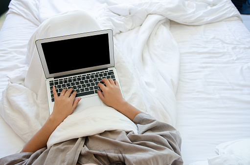 Woman waer robe wrap with blanket using the laptop on her bed