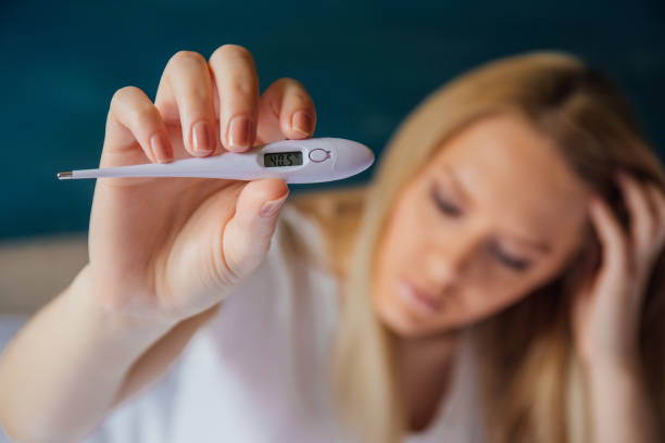 istock Woman with fever holding thermometer 972578896