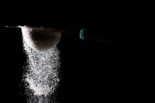 istock Flour sifting on a black background. White powder sift isolated on black background 972596940