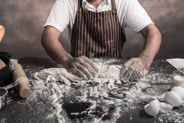 istock Man preparing buns at table in bakery, Man sprinkling flour over fresh dough on kitchen table 972617300