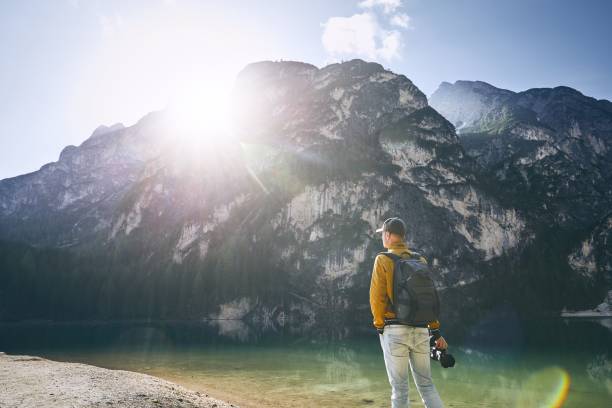 Young photographer holding camera against Lake Braies and mountains during sunrise. Dolomites, Italy