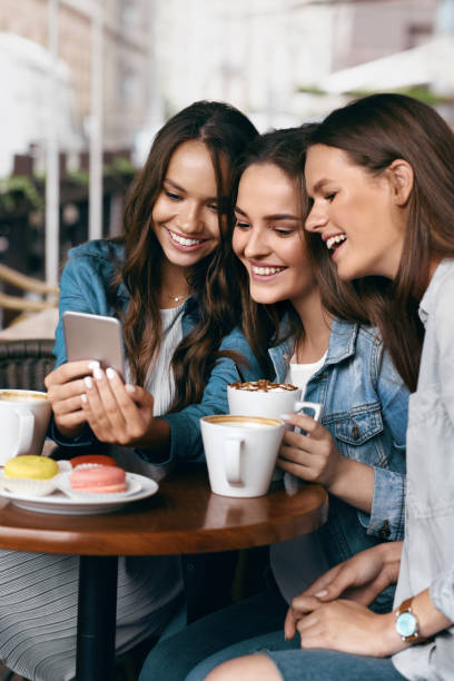 istock Young Female Friends Using Phone And Drinking Coffee In Cafe. 972654872