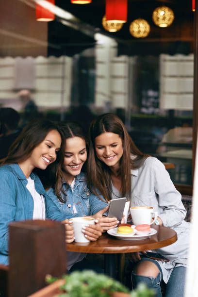 istock Young Female Friends Using Phone And Drinking Coffee In Cafe. 972655316
