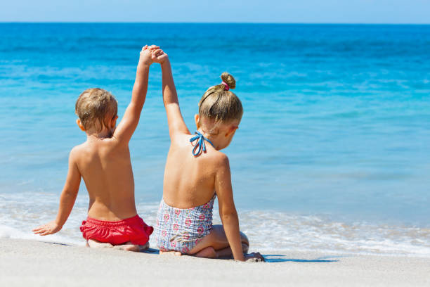 Happy kids have fun in summer camp on beach vacations Happy kids have fun in sea surf on white sand beach. Couple of children sit in water pool with hands up. Travel lifestyle, swimming activities in family summer camp. Vacations on tropical island. summer camp photos stock pictures, royalty-free photos & images