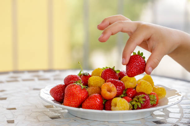 istock child hand taking bio yellow raspberries and red strawberries. close up 972709750