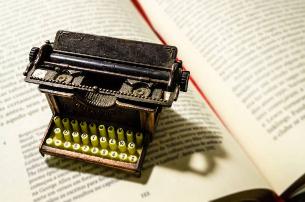 small typewriter in copper tones in focus on a page of an old book. decoration item. concept of reading, writing, old times, past. - typewriter sepia toned old nostalgia imagens e fotografias de stock