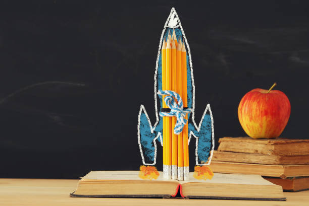 istock Bck to school concept. rocket sketch and pencils over open book in front of classroom blackboard. 972719390