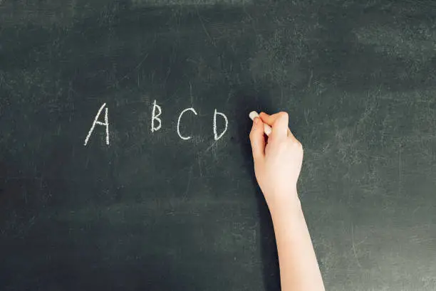 Photo of child's hand with chalk write alphabet on black chalkboard