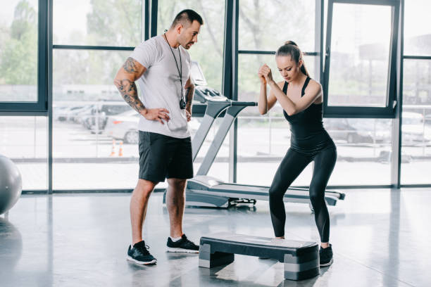 istock young athletic woman doing step aerobics exercise and male personal trainer at gym 972728548