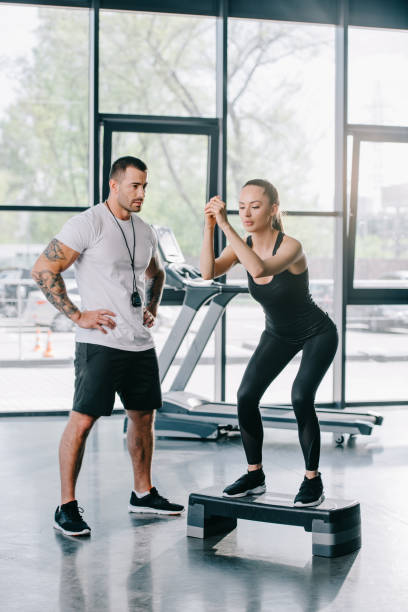 istock male personal trainer and young sportswoman doing step aerobics exercise at gym 972728664