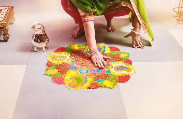 Women coloring tradition colorful rice art or sand art (Rangoli) on the floor with paper pattern using dry rice and dry flour with colored from natural pigments like sindoor, haldi (turmeric)
