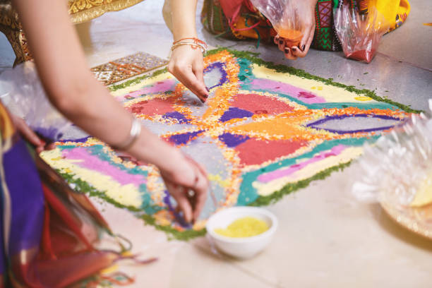 Bride's friend helps coloring the traditional rice art (Rangoli) on the floor for indian wedding Women helps coloring tradition colorful rice art or sand art (Rangoli) on the floor with paper pattern using dry rice and dry flour with colored from natural pigments like sindoor, haldi (turmeric) haldi ceremony stock pictures, royalty-free photos & images