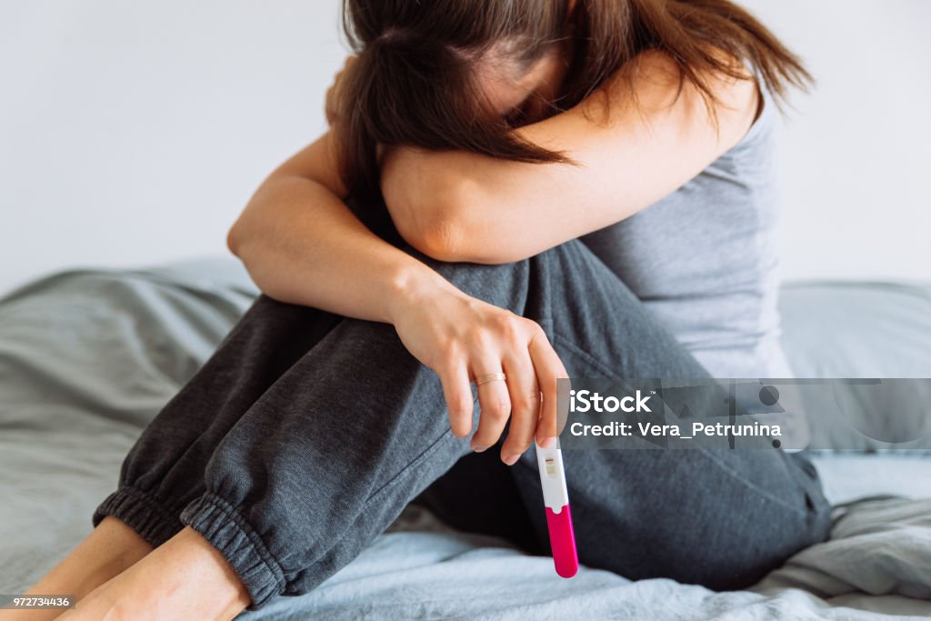 sad woman on bed with negative pregnancy test Infertility Stock Photo