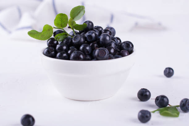 istock Fresh blueberries with green leaf  in a white bowl on a white background 972742314