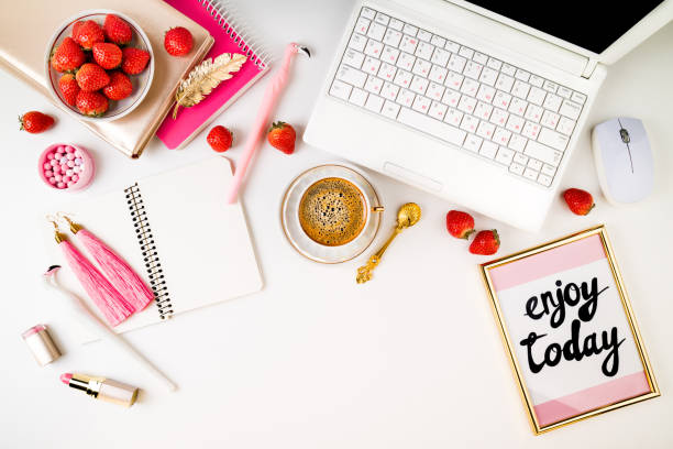 Trendy feminine home workplace. Home office desk with laptop, notebook, fresh strawberries, cosmetics, accessories and coffee cup on white background. Flat lay