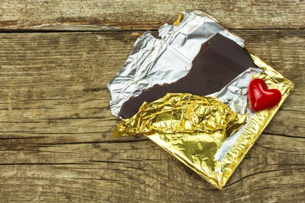 istock Bitter chocolate in a gold foil on a wooden board. Chocolate delicacy. 972766598