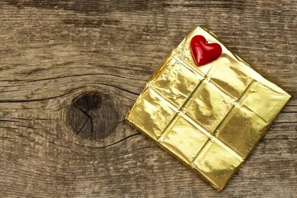 Bitter chocolate in a gold foil on a wooden board. Chocolate delicacy